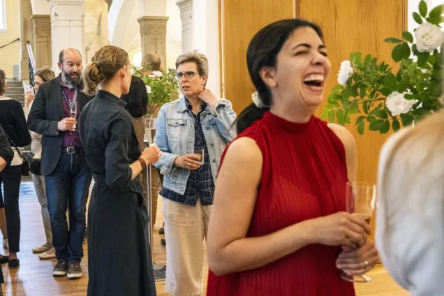 En folksamling minglar och en skrattande ung kvinna i förgrunden. Foto.